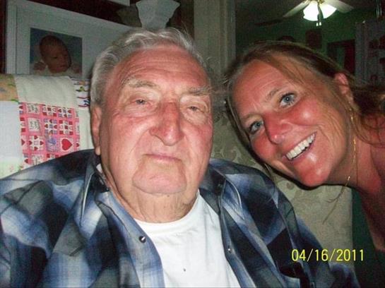 An elder man poses with a smiling young woman during a lively family gathering at home.