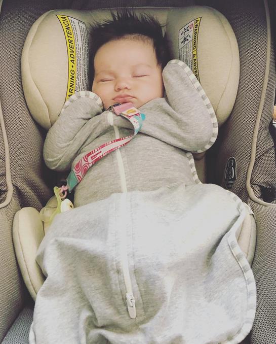 A calm baby rests in a car seat, wrapped in a blanket, enjoying the ride during daytime travel.