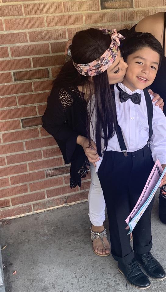 A child dressed in formal clothing is embraced and kissed by an adult, showcasing warmth and love.