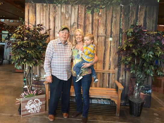 Three family members pose together in a cozy indoor area with wooden decor.
