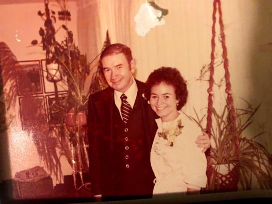 A couple stands close, smiling joyfully in a charming room adorned with greenery and soft lighting.