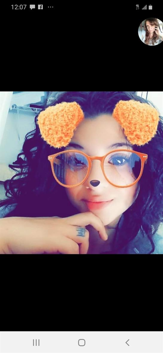 A young woman with curly hair and playful glasses poses thoughtfully, enjoying herself.
