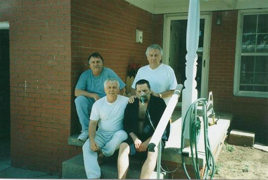 Four friends enjoy a relaxed moment on the steps of a brick house on a sunny day.