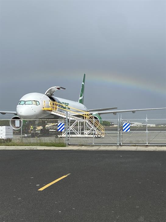 An airplane is at an airport gate under cloudy skies with a rainbow in the background.