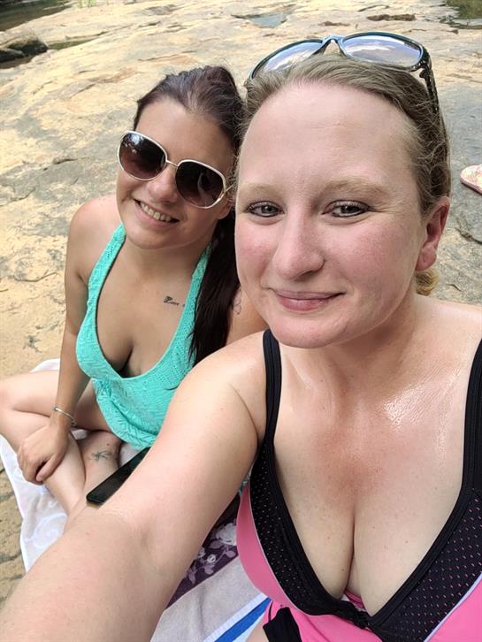 Two friends sit together by the water, enjoying a sunny day and each other's company.