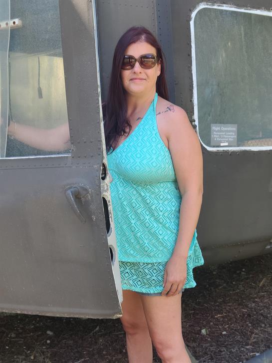 A woman in a turquoise dress and sunglasses stands by a retro camper on a sunny day.