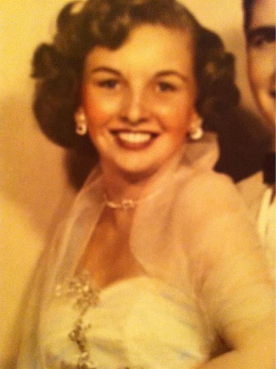 A cheerful young woman in formal attire with curly hair and earrings at a special event.