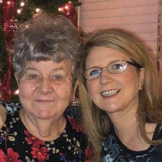 Two women share smiles in a festive indoor space decorated for the holidays.