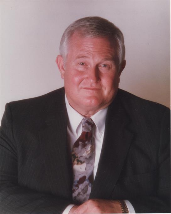 A smiling man in a suit and tie presents a confident expression in a studio setting.