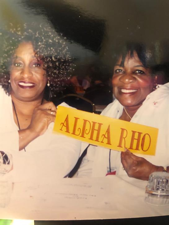 Two joyful women hold up a banner at a sorority gathering, celebrating sisterhood and friendship.