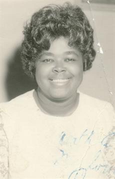 A joyful woman with curly hair poses for a portrait, showcasing her bright smile and warm demeanor.