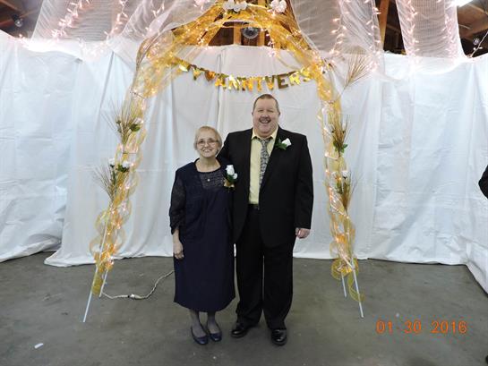Elderly couple smiles together beneath a beautiful arch decorated for a special occasion.