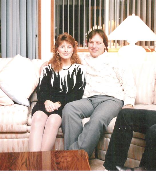 A couple relaxes on a comfortable couch in a warmly decorated living room, smiling together.