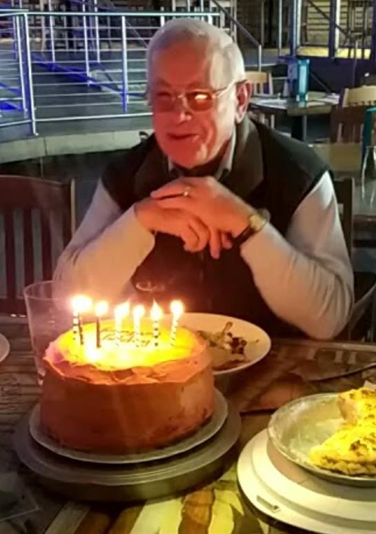 A man enjoys his birthday cake surrounded by friends while candles are lit.