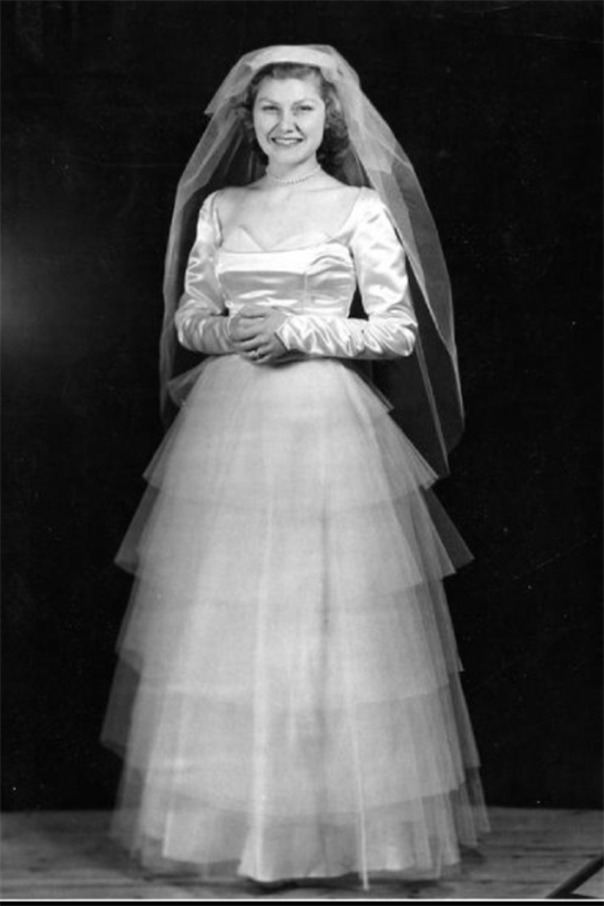 Woman stands gracefully in a layered wedding gown, showcasing classic bridal elegance with a veil.