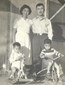 Two adults stand behind two children, one on a bike and the other holding a toy, smiling happily.