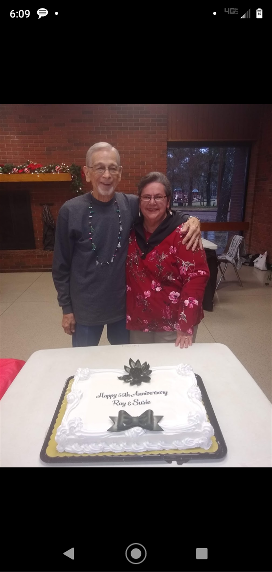 Ray and Suzie proudly celebrate their anniversary with loved ones beside their cake.