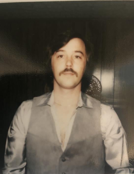 A young man in a stylish vest and mustache stands confidently in a vintage interior.