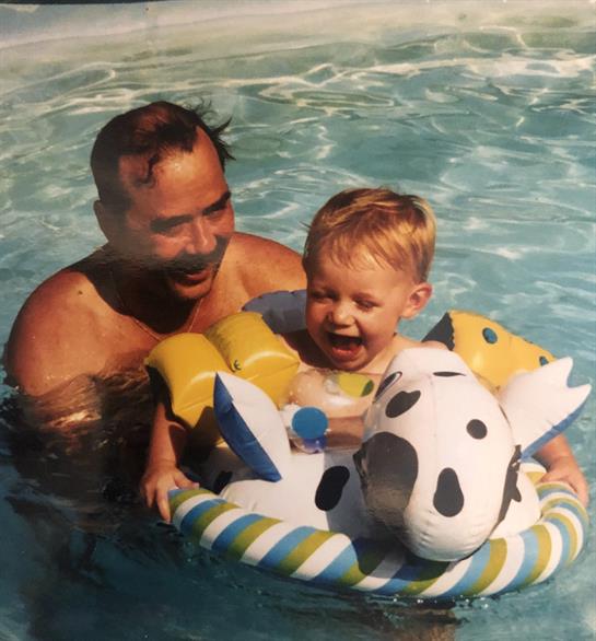 A joyful child is swimming with his father in a pool, laughing and playing with inflatable toys.