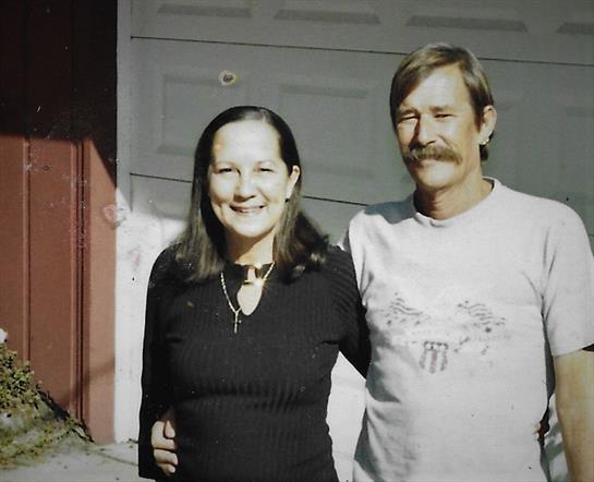 Two smiling individuals stand together in front of a garage, enjoying their time outdoors.