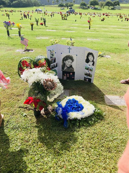 Flowers and pictures are laid at a memorial site during a sunny day, honoring loved ones.