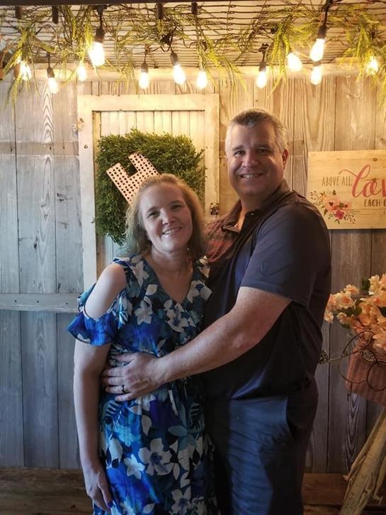 A couple joyfully embraces in a beautifully decorated space with lights and flowers.