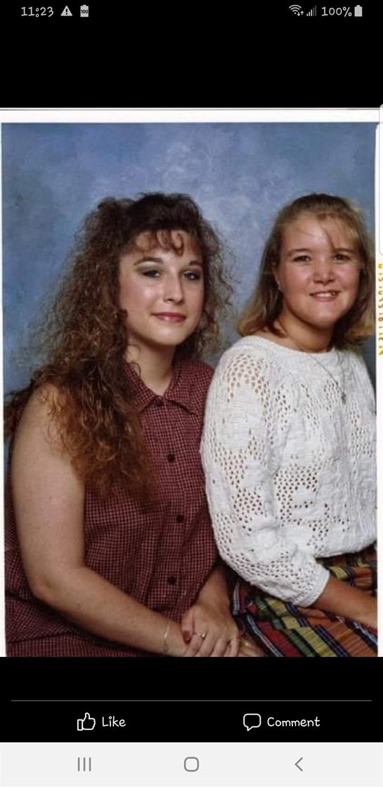 Two young women pose closely, smiling at the camera in a professional studio environment.