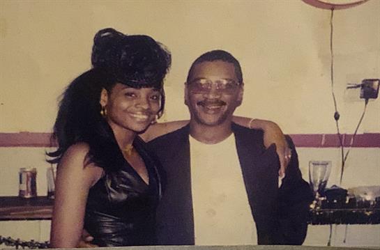 A joyful couple poses closely, sharing smiles and warmth at a vibrant event, dressed elegantly.