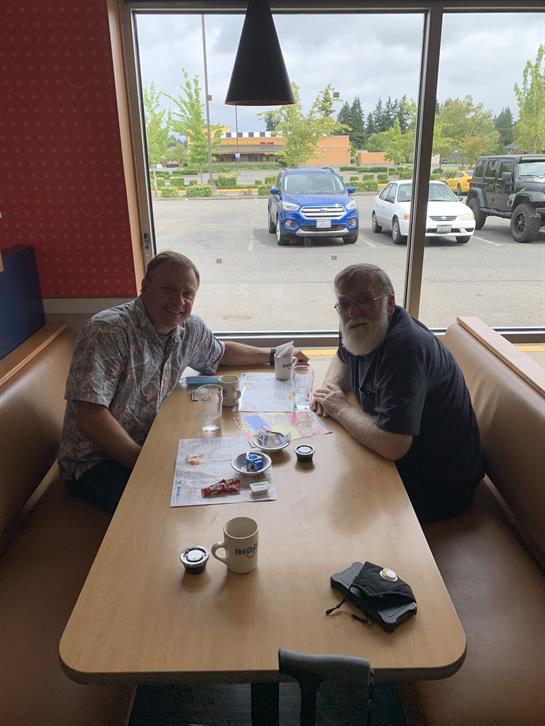 Two men chat over coffee at a cafe, enjoying the view.