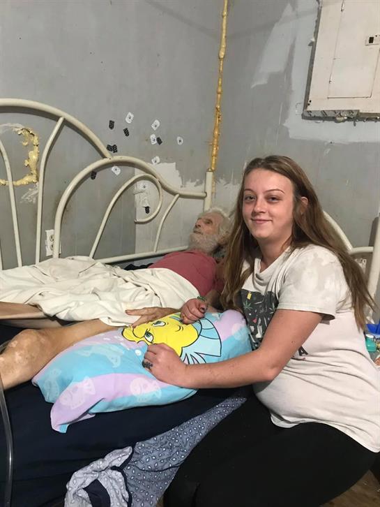 A young woman provides comfort to her elderly relative in a modest bedroom.