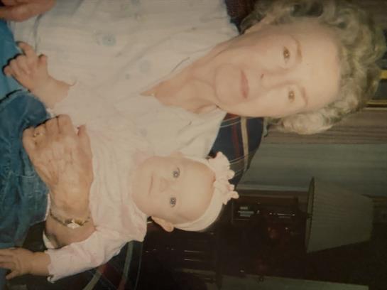 An elderly woman lovingly holds a baby in her arms in a warm home setting.