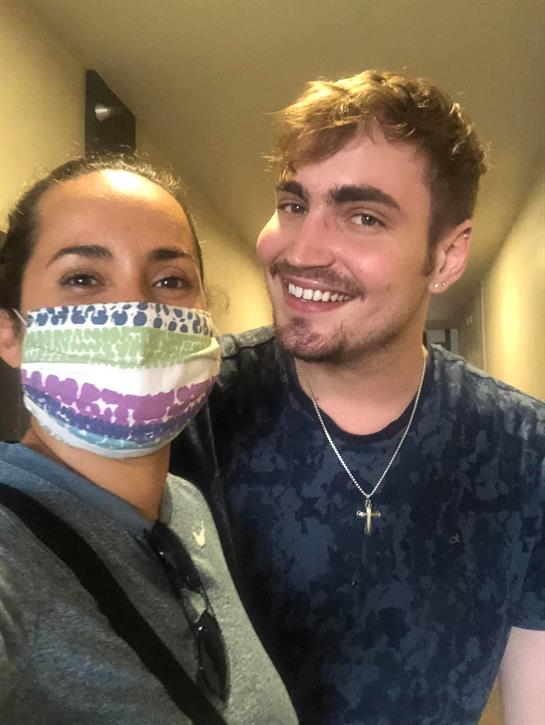 Two people share a joyful moment indoors, both wearing colorful face masks and smiling warmly.
