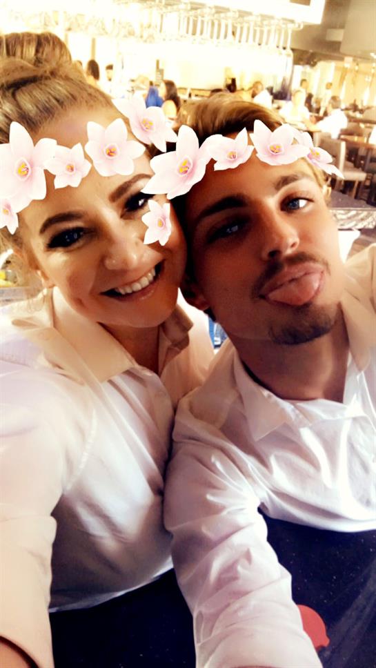 Two friends smile and pose with floral crowns in a cheerful, lighthearted scene.