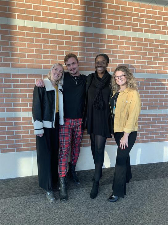 Four friends stand closely together, enjoying a moment in natural light near a brick wall.