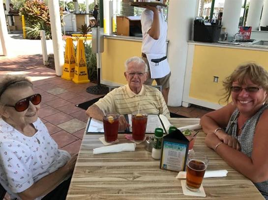 Three people enjoy refreshments at a coastal restaurant, sharing laughs and stories together.