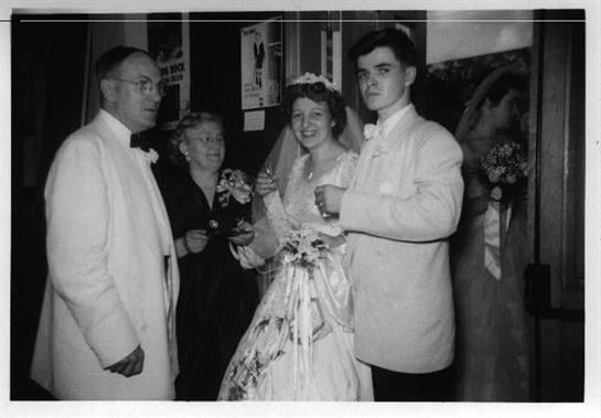 A couple poses in wedding attire with guests, sharing joy and drinks during the celebration.