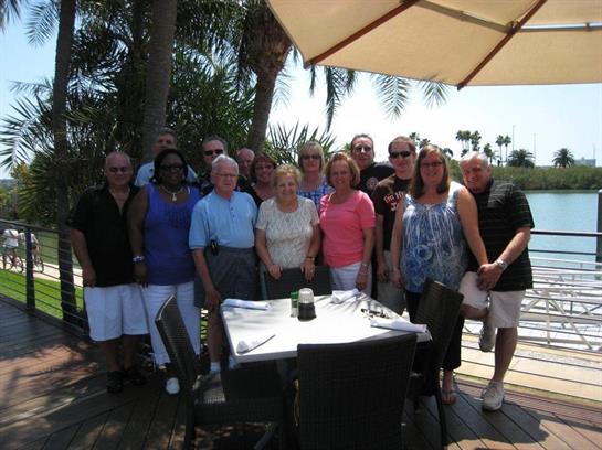 A happy group of friends gathers at a sunny table surrounded by palm trees.