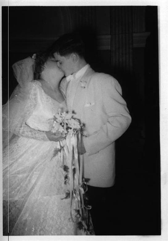 A couple embraces and kisses beneath soft lighting, celebrating their wedding day joyfully.