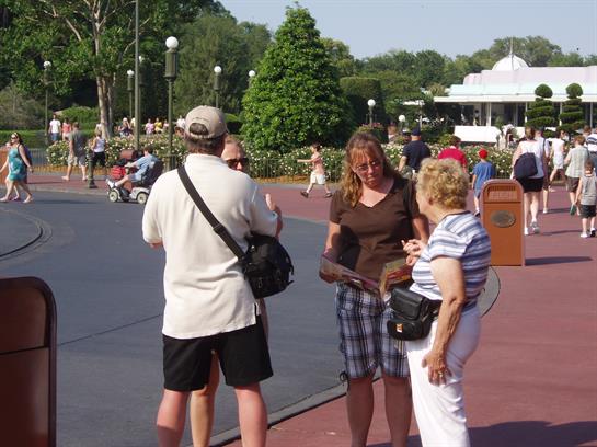 Group of three people chat and share laughs in a lively park filled with visitors.