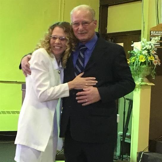 A happy couple embraces in formal wear, capturing a joyful moment in a vibrant indoor space.