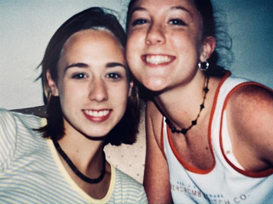 Two young friends pose for a cheerful snapshot, enjoying time together at a gathering.