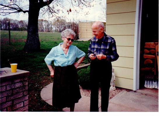 An elderly couple shares a joyful moment outside, surrounded by vibrant greenery, during spring.