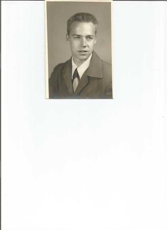 A young man dressed in a formal suit and tie poses confidently in a vintage studio setting.