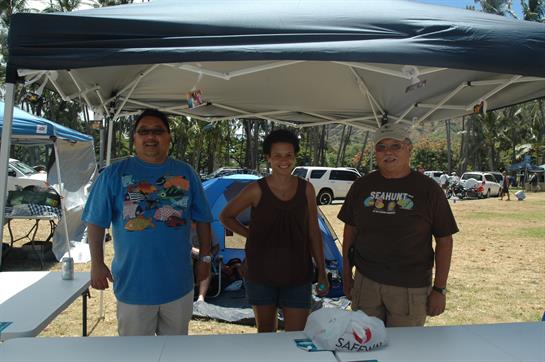 Three friends relax under a tent at a beach gathering, smiling and enjoying their time together.