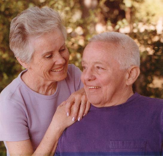 Two elderly individuals smile at each other, enjoying a heartwarming moment in a garden.