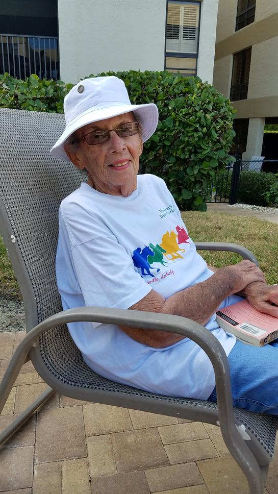 Senior woman sits in a chair reading a book while enjoying a sunny day at a park.