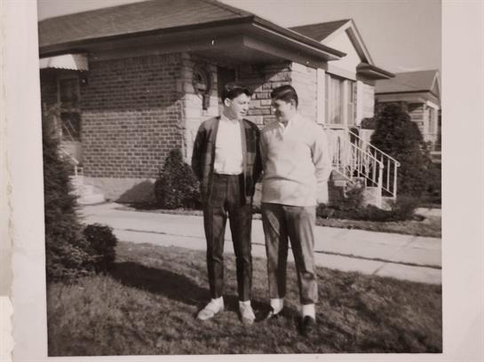Two young men share a moment outside their homes as they enjoy a sunny day in the 1960s.