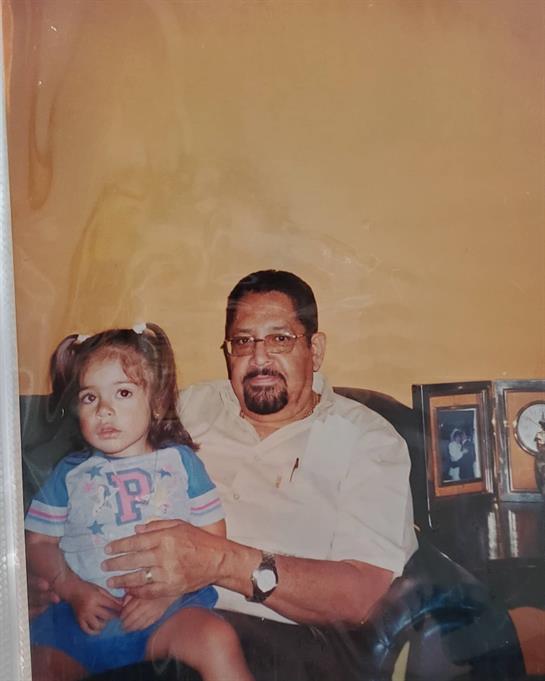 A man smiles at the camera while holding a young girl on his lap, showcasing a family moment.