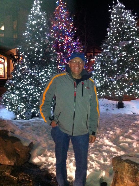 A man is enjoying a winter evening walk surrounded by brightly lit trees and snow.