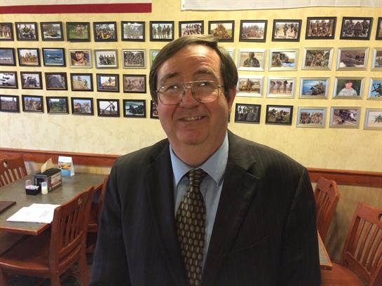 A friendly man wearing glasses and a suit poses in a cozy restaurant decorated with framed pictures.